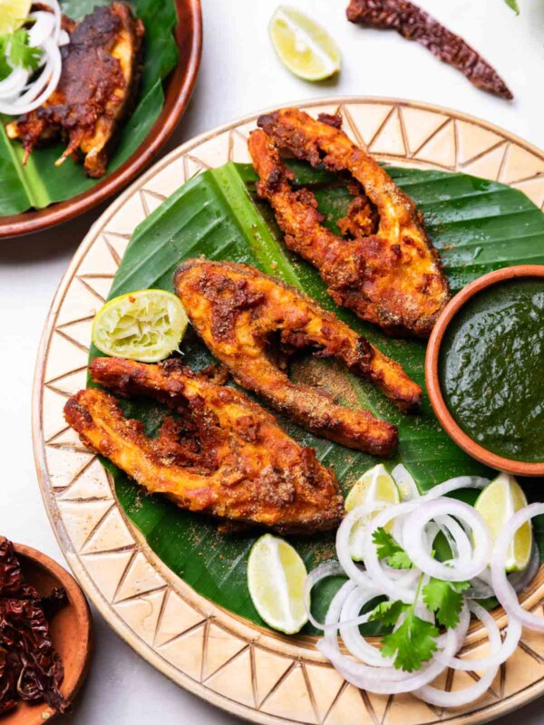 Amritsari fish fry served on a leaf platter with green chutney, onion slices, and lemon wedges