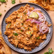 an image of chicken bharta served with sliced onion and lemon wedges
