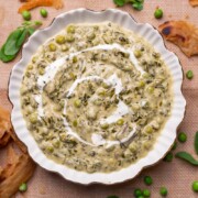 Methi Matar Malai served in a white bowl with lachha paratha, fenugreek leaves, matar etc strewn about