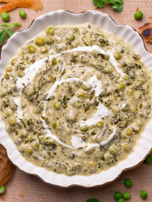 Methi Matar Malai served in a white bowl with lachha paratha, fenugreek leaves, matar etc strewn about