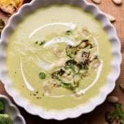 broccoli almond soup served in a white bowl with accompaniments