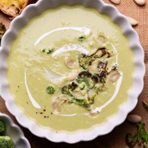broccoli almond soup served in a white bowl with accompaniments