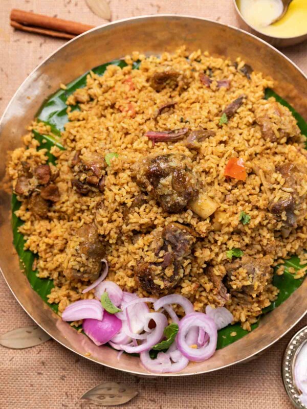 dindigul mutton biryani served on a copper plate with accompaniments