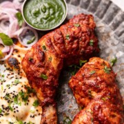 tandoori chicken served on a plate with naan, chutney, and sliced onions