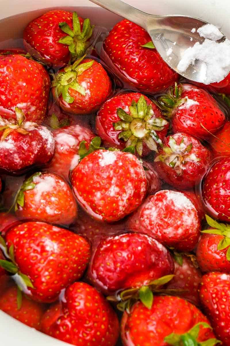 a close up image of strawberries soaked in water with a sprinkling of baking powder