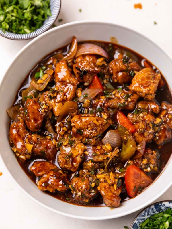 chicken manchurian served in a white bowl accompanied with garnishings
