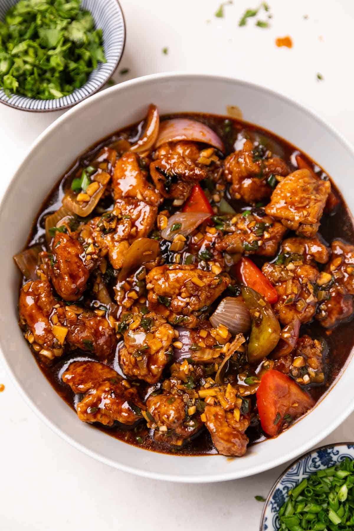 chicken manchurian served in a white bowl accompanied with garnishings