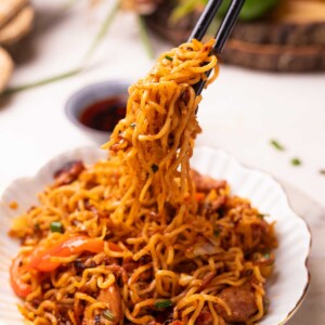 an image of chilli chicken noodles picked up with a pair of chopsticks
