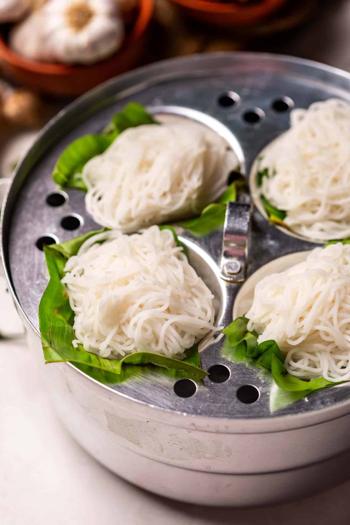 Rice Idiyappam pictured in a steamer over banana leaf