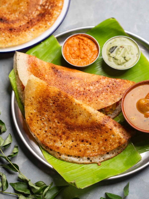 freshly made dosas served on a banana leaf platter with accompaniments