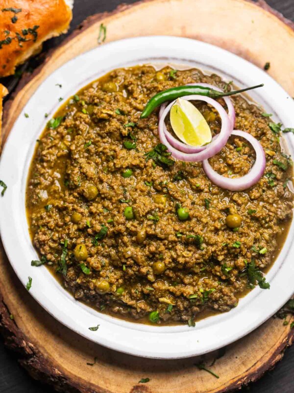 green keema masala served in a white bowl with onion rings, slit green chillies, and a lemon wedge