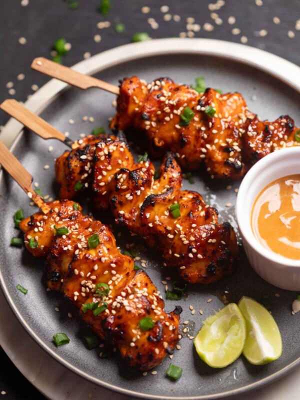 an image of bang bang chicken skewers served on a black platter with accompaniments