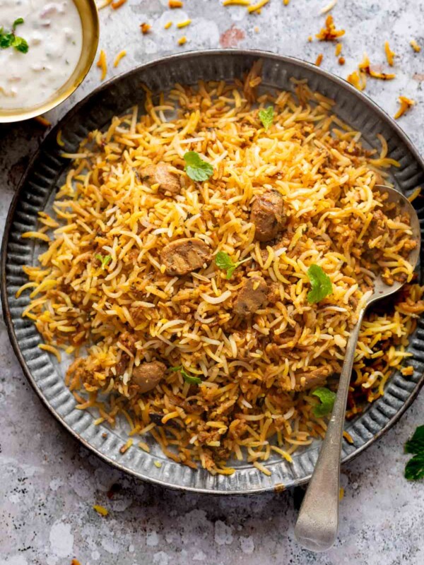 A plateful of mushroom biryani with a spoon on the side and a bowl of raita