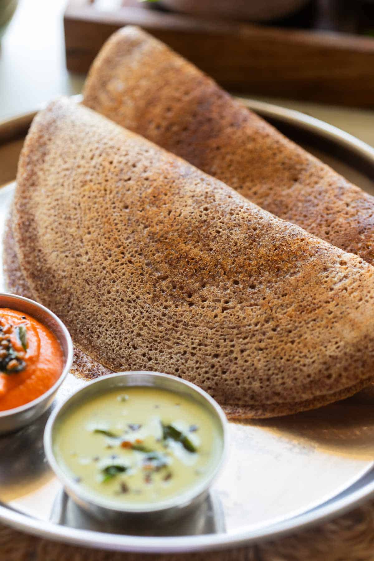 an image of fluffy and crispy ragi dosas served with accompaniments