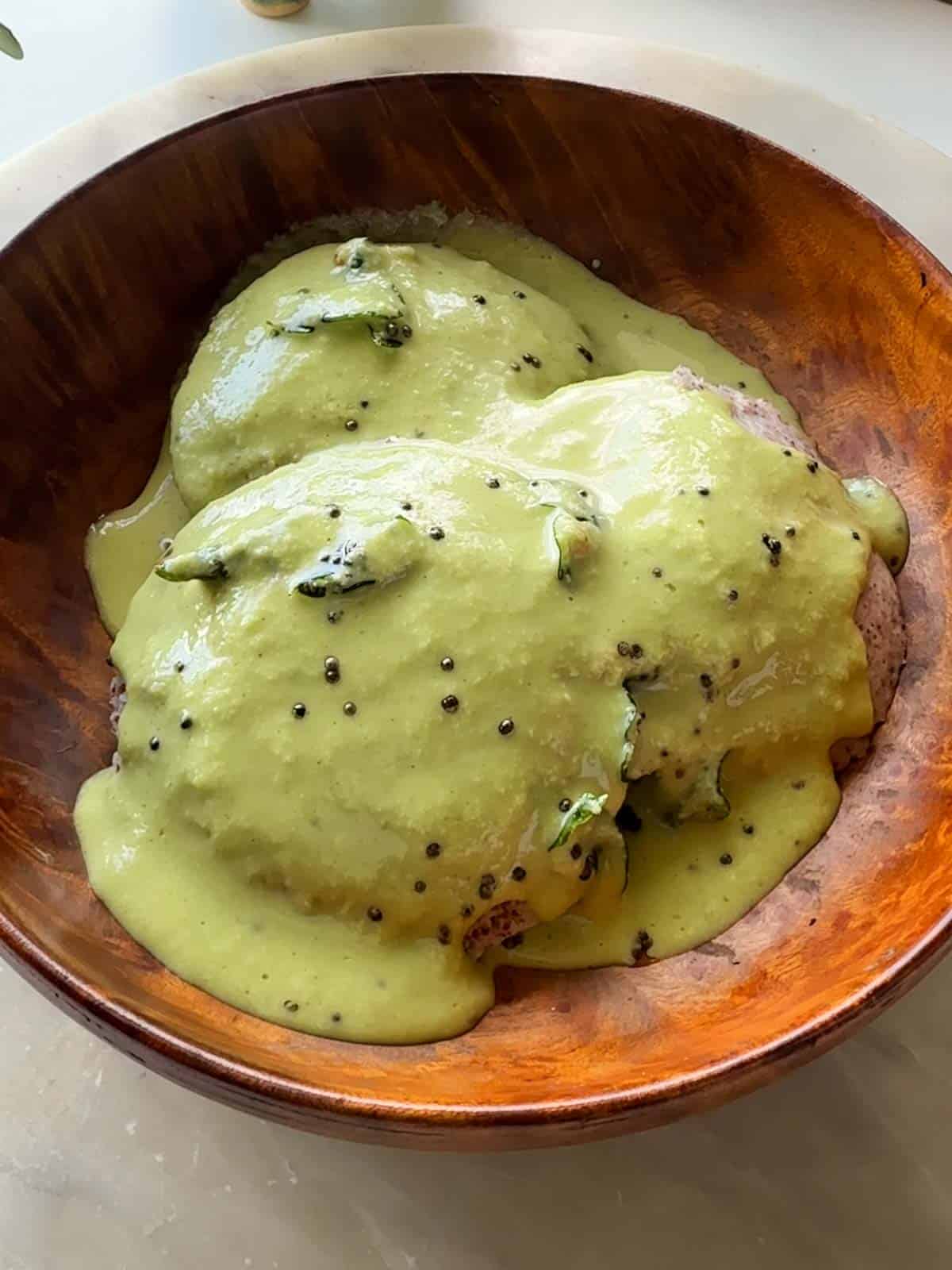 an an image of ragi idlis with chutney poured over and served in a wooden bowl
