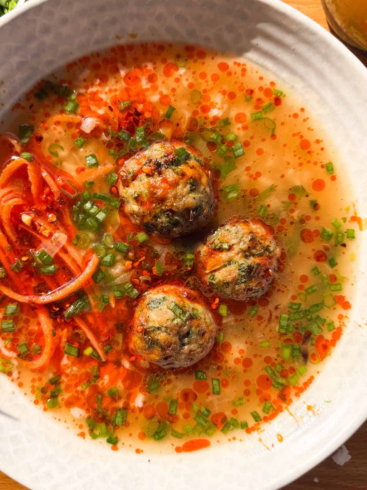 close up image of air fryer chicken meatballs in ginger broth to showcase it's texture and color