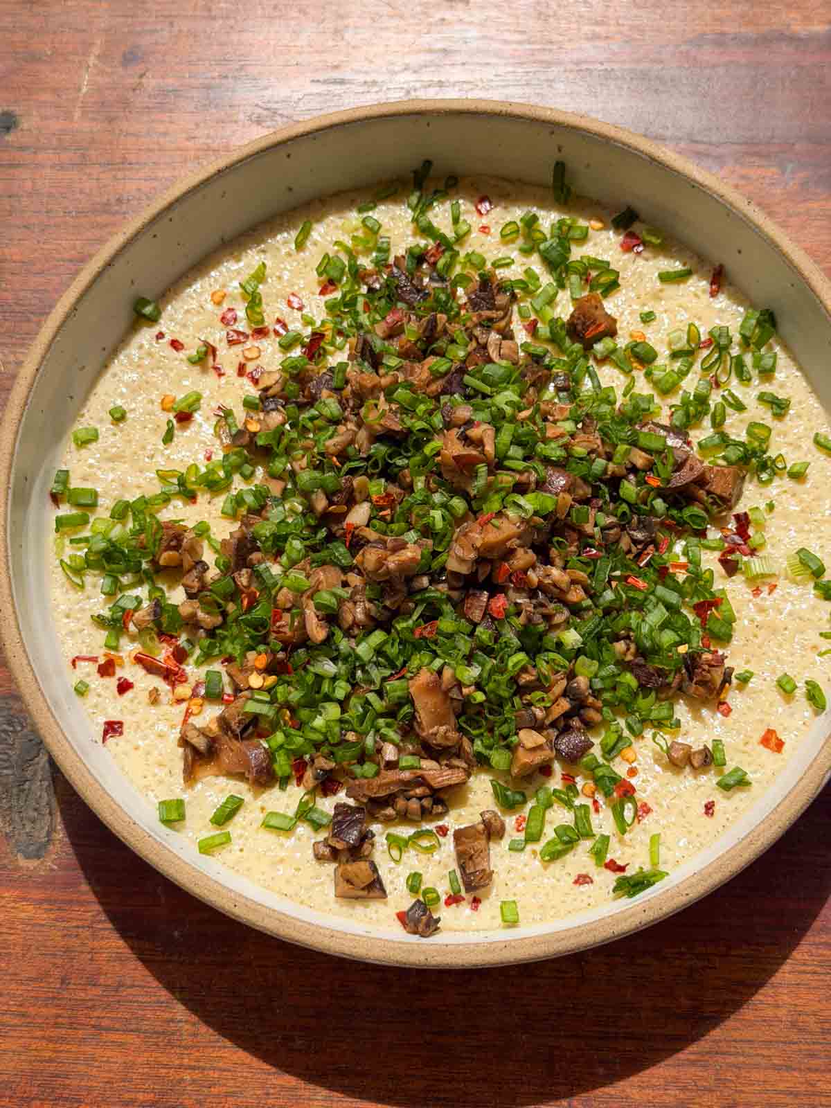 an image of chinese steamed eggs garnished with mushroom and spring onion ready to be eaten